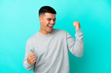 Soyutlanmış mavi arka planda genç yakışıklı bir adam zaferi kutluyor.