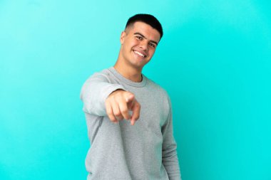 Soyutlanmış mavi arka planda genç yakışıklı adam mutlu bir ifadeyle öne bakıyor.