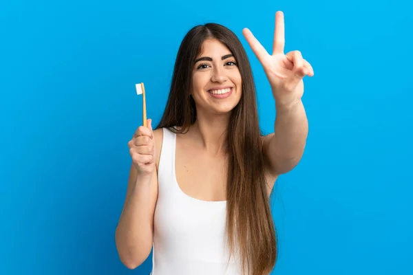 Młoda Biała Kobieta Myje Zęby Odizolowane Niebieskim Tle Uśmiechając Się — Zdjęcie stockowe