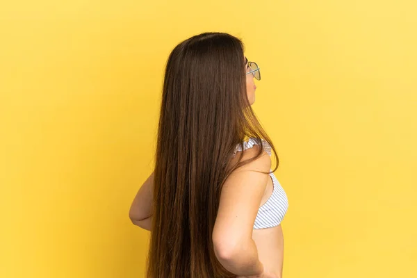 在暑假穿泳衣的年轻的高加索女人因努力工作而因背痛而被隔离在黄色背景之外 — 图库照片