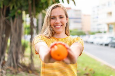 Açık havada elinde portakal tutan genç sarışın kadın.
