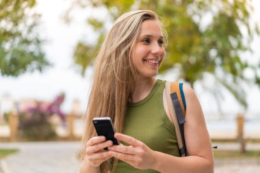 Açık havada cep telefonu kullanan genç sarışın kadın.