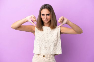 Mor arka planda izole edilmiş beyaz bir kadın baş parmağını iki eliyle aşağı gösteriyor.