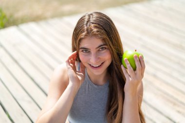 Genç, güzel, beyaz bir kadın elinde mutlu bir ifadeyle bir elma tutuyor.