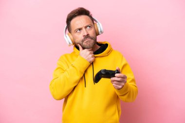 Orta yaşlı bir adam pembe arka planda izole edilmiş bir video oyunu kontrolörüyle oynuyor.