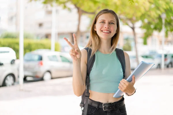 Junge Blonde Studentin Lächelt Und Zeigt Siegeszeichen — Stockfoto