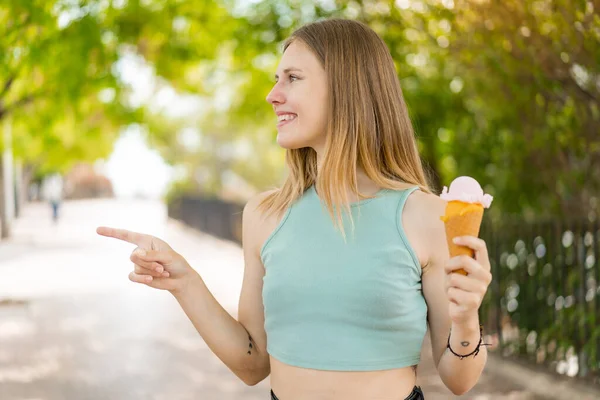 stock image Young blonde pretty woman with a cornet ice cream at outdoors pointing to the side to present a product