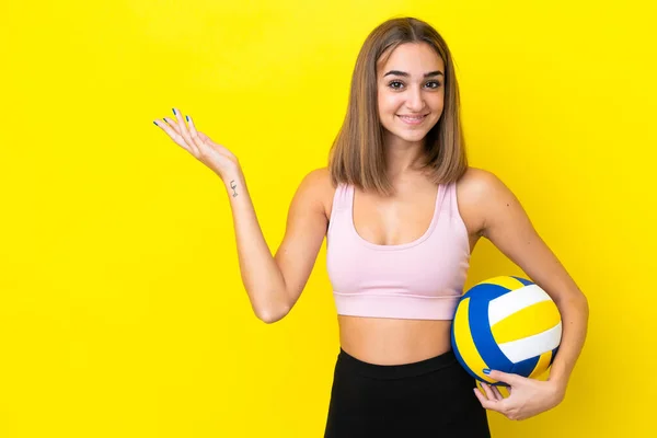 年轻女子打排球是在黄色背景下隔离开来的 她向旁边伸出手来邀请人来 — 图库照片
