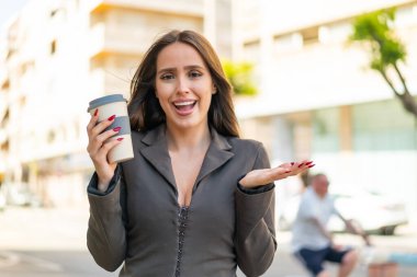 Dışarıda elinde kahve tutan genç bir kadın şok olmuş bir yüz ifadesiyle.
