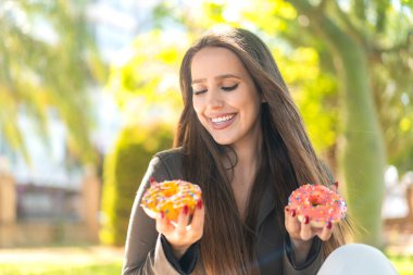 Açık havada elinde mutlu bir ifadeyle donut tutan genç bir kadın.