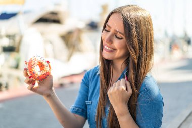 Dışarıda elinde donut tutan genç bir kadın zaferi kutluyor.