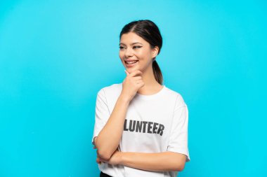 Genç Rus gönüllü kız mavi arka planda izole edilmiş. Yan tarafa bakıyor ve gülümsüyor.