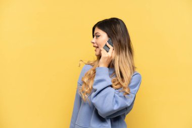 Sarı arka planda izole edilmiş genç bir Rus kızı cep telefonuyla sohbet ediyor.