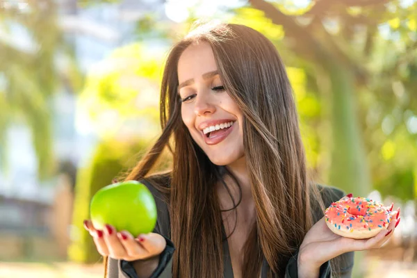 Молодая Женщина Открытом Воздухе Держит Яблоко Пончик Счастливым Выражением Лица — стоковое фото