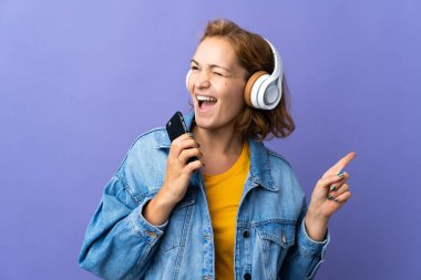 Genç Gürcü kadın, mor arka planda izole edilmiş. Cep telefonuyla müzik dinliyor ve şarkı söylüyor.