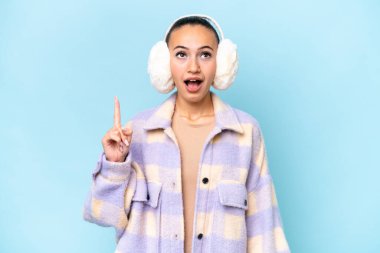 Mavi arka planda izole edilmiş kışlık kuklalar giyen genç bir Arap kadını işaret ediyor ve şaşırtıyor