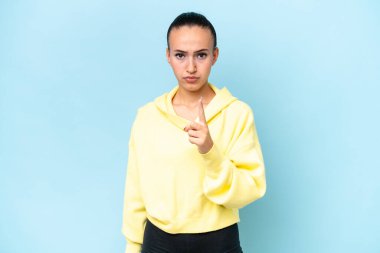 Mavi arka planda izole edilmiş genç bir Arap kadın hayal kırıklığına uğramış ve ön tarafı işaret ediyor.