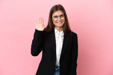 Genç beyaz kadın pembe arka planda izole edilmiş, mutlu bir ifadeyle selamlanıyor.