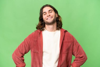 Soyutlanmış arka planda genç yakışıklı adam kolları kalçasında ve gülümsüyor.