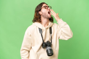 İzole edilmiş arka planda genç fotoğrafçı esniyor ve elleriyle ağzını kapatıyor.