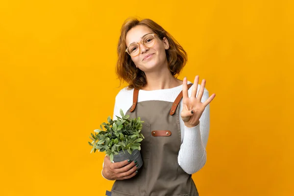 一位年轻的格鲁吉亚妇女高高兴兴地抱着一棵黄色背景的植物 用手指数着四棵 — 图库照片