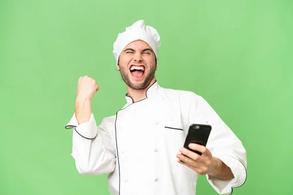 Jonge Knappe Chef Kok Man Geïsoleerde Achtergrond Met Telefoon Overwinningspositie — Stockfoto