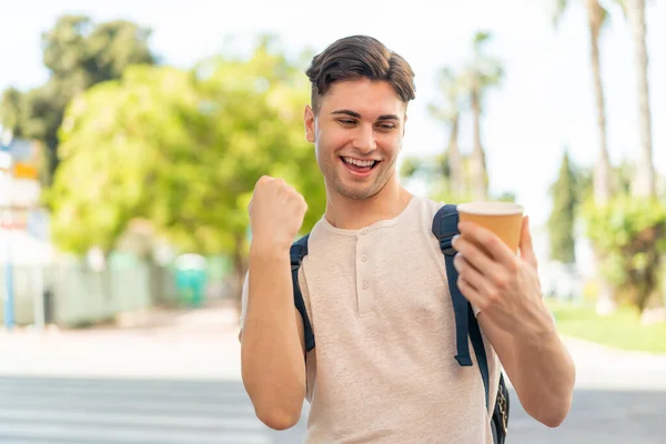 年轻英俊男子在户外拿着咖啡庆祝胜利 — 图库照片