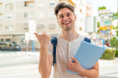 Dışarıdaki yakışıklı öğrenci bir ürün sunmak için yan tarafı işaret ediyor.