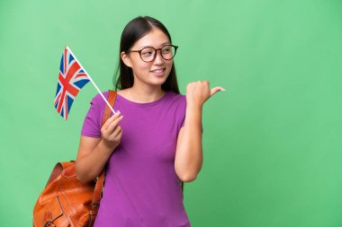 Young Asian woman holding an United Kingdom flag over isolated background pointing to the side to present a product