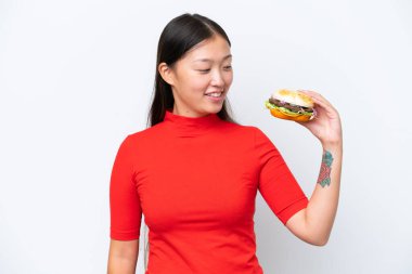 Young Asian woman holding a burger isolated on white background with happy expression