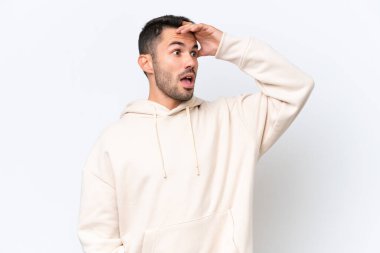 Beyaz arka planda izole edilmiş genç beyaz adam yan tarafa bakarken sürpriz jest yapıyor.