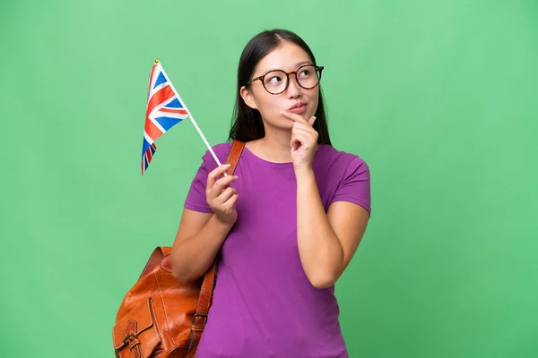 在孤立的背景下举着英国国旗向上看的年轻亚洲妇女 — 图库照片