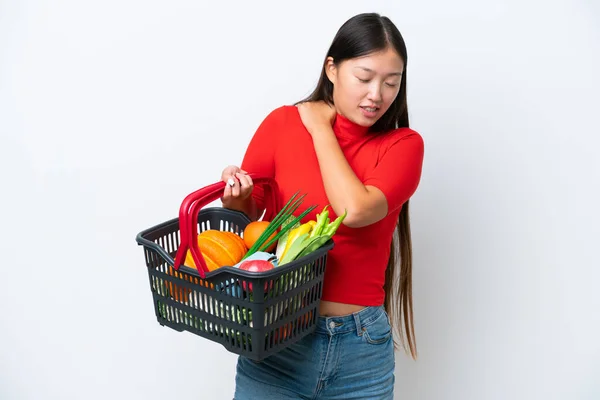 年轻的亚洲女人提着一个购物篮 里面装满了被白色背景隔离的食物 肩负着痛苦 因为她付出了巨大的努力 — 图库照片