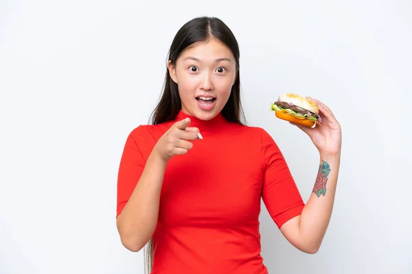 Młoda Azjatka Trzyma Hamburgera Odizolowany Białym Tle Zaskoczony Wskazując Przodu — Zdjęcie stockowe