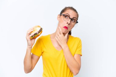Young caucasian woman holding a burger isolated on white background having doubts