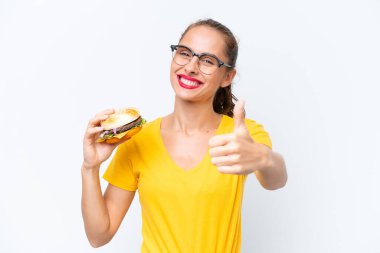 Beyaz arka planda iyi bir şey olduğu için izole edilmiş beyaz bir hamburger tutan genç beyaz kadın.