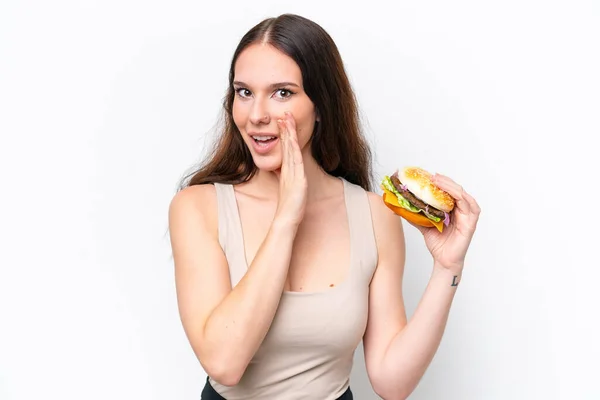 Młoda Biała Kobieta Trzyma Hamburgera Białym Tle Szepcząc Coś — Zdjęcie stockowe