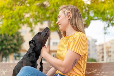 Dışarıda sevimli siyah köpeği olan genç sarışın kadın.