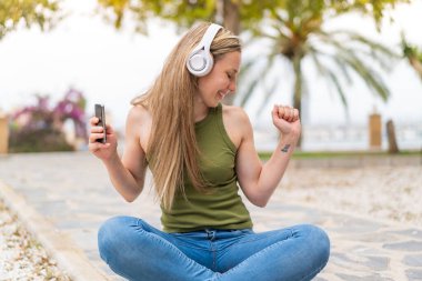 Açık havada cep telefonu kullanan genç sarışın kadın.