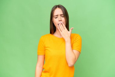 Genç, beyaz bir kadın izole edilmiş arka planda esniyor ve ağzını eliyle kapatıyor.