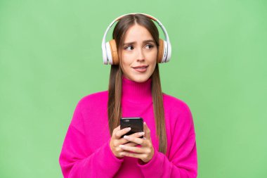 Genç, güzel, beyaz bir kadın izole edilmiş arka planda müzik dinliyor ve düşünüyor.