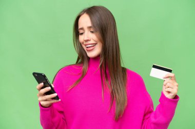 Young beautiful caucasian woman over isolated background buying with the mobile with a credit card