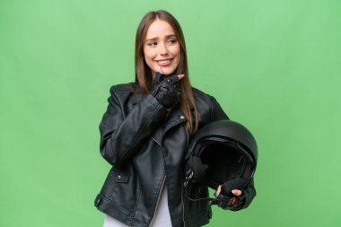 Motosiklet kasklı, izole edilmiş arka planda genç, beyaz bir kadın yana bakıyor ve gülümsüyor.