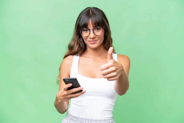 stock image Young caucasian woman over isolated background using mobile phone while doing thumbs up