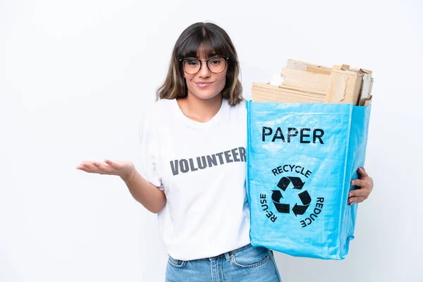 白い背景で隔離された紙をリサイクルするためにリサイクルバッグを持っている若い白人女性は肩を持ち上げながら疑問ジェスチャーを作ります — ストック写真