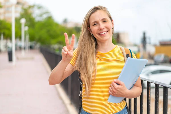 Junge Blonde Studentin Lächelt Und Zeigt Siegeszeichen — Stockfoto