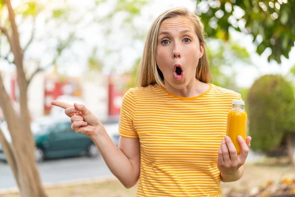 Mladá Blondýnka Drží Pomerančový Džus Venku Překvapen Ukazuje Stranou — Stock fotografie
