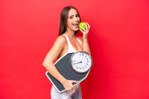 Young Beautiful Caucasian Woman Isolated Red Background Weighing Machine Apple — Fotografia de Stock