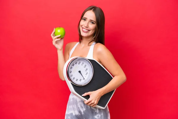 Young Beautiful Caucasian Woman Isolated Red Background Weighing Machine Apple — стоковое фото