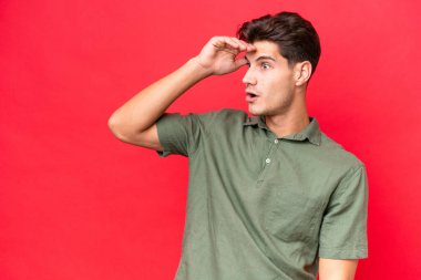 Beyaz, yakışıklı genç bir adam, kırmızı arka planda yalnız ve yana bakarken şaşırmış bir ifadeyle.